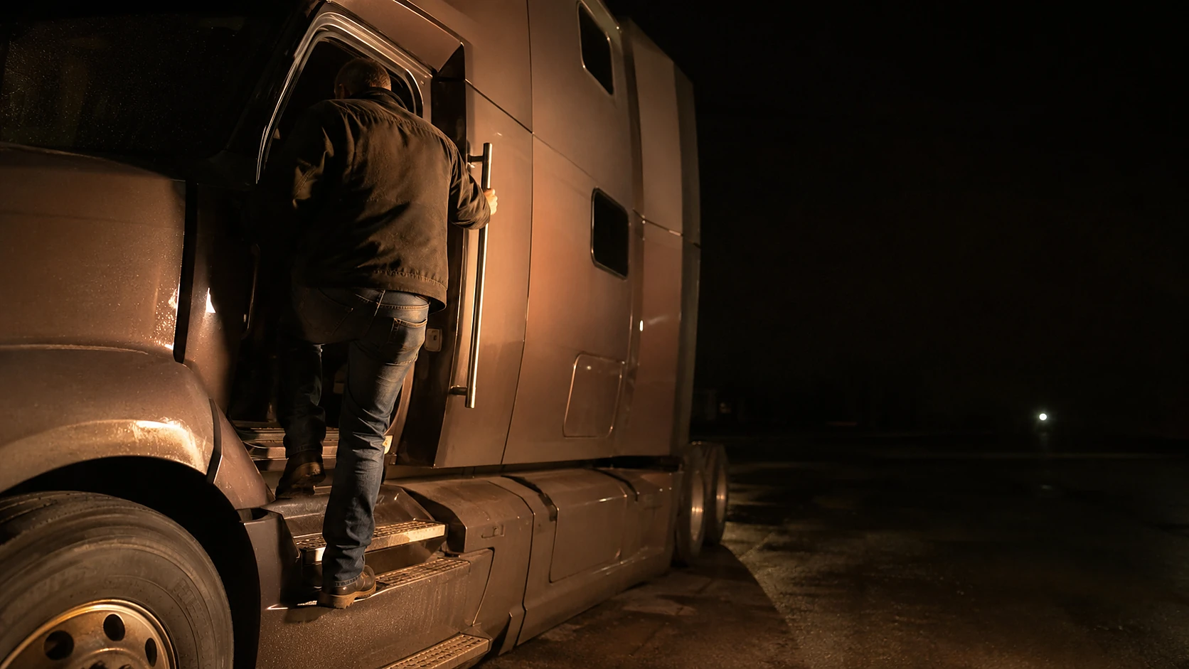 A driver stepping up into his truck cab before dawn at an empty lot.